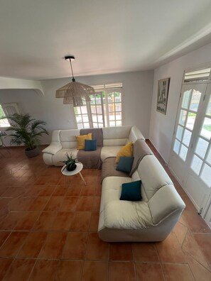 A living room with a sectional sofa, a hanging light fixture, and a potted plant. - VILLA CLIANE (Baie-Mahault)