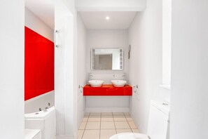 Baño con dos lavamanos, un espejo y una pared de acento en rojo.
