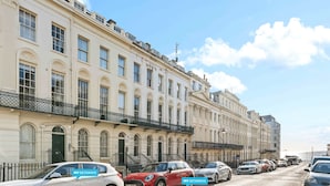 A row of classic European townhouses with uniform architectural style, a clear sky, and parked cars along the street. - Oriental Eight | By My Getaways (Brighton)