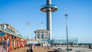 A tall tower with a circular observation deck, a covered walkway with shops, and a clear blue sky. - Oriental Eight | By My Getaways (Brighton)
