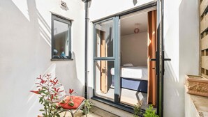 A small room with a sliding glass door leading to an outdoor area, a window, and a chair with a cushion. - Chapel Waves | By My Getaways (Brighton)