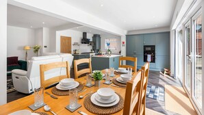 A modern kitchen with grey cabinets, a dining area with a wooden table set for four, and a living area with a white sofa. - Coral Haven With Parking | By My Getaways (Worthing)