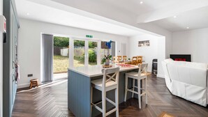 A modern kitchen with a central island, a dining area with chairs, a white sofa, and a Netflix sign. - Coral Haven With Parking | By My Getaways (Worthing)