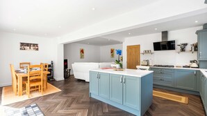 A modern kitchen with a dining area, wooden furniture, and a blue island. - Coral Haven With Parking | By My Getaways (Worthing)