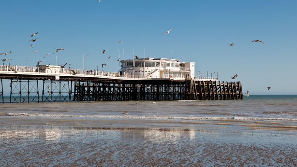 A pier extending into the water with a building at the end, surrounded by birds. - Coral Haven With Parking | By My Getaways (Worthing)