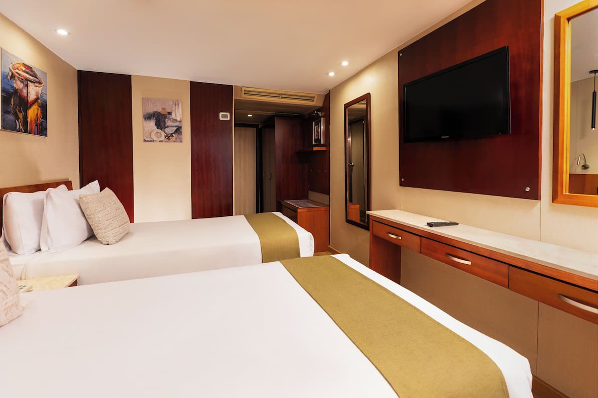 A hotel room with two beds, a TV, a desk, and a mirror.
