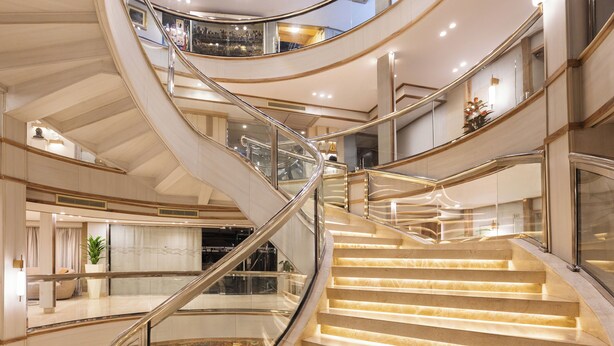 Et flerplansinteriør med en buet trappe, glasgelændere og et godt oplyst atrium.