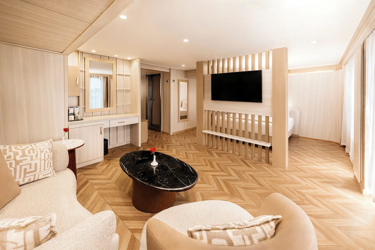 A modern hotel room with a large TV, a sofa, a coffee table, and a wooden floor.