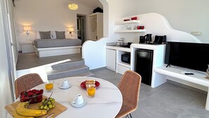 Quarto de hotel moderno com cama, cozinha compacta, área de refeições e televisão.