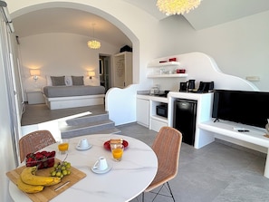 A modern hotel room with a bed, kitchenette, dining area, and a TV. - Villa Koralya (Episkopi Gonias)
