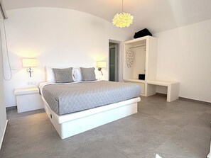 A bedroom with a bed, bedside lamps, a bench, a walk-in closet, and a hanging light fixture. - Villa Koralya (Episkopi Gonias)