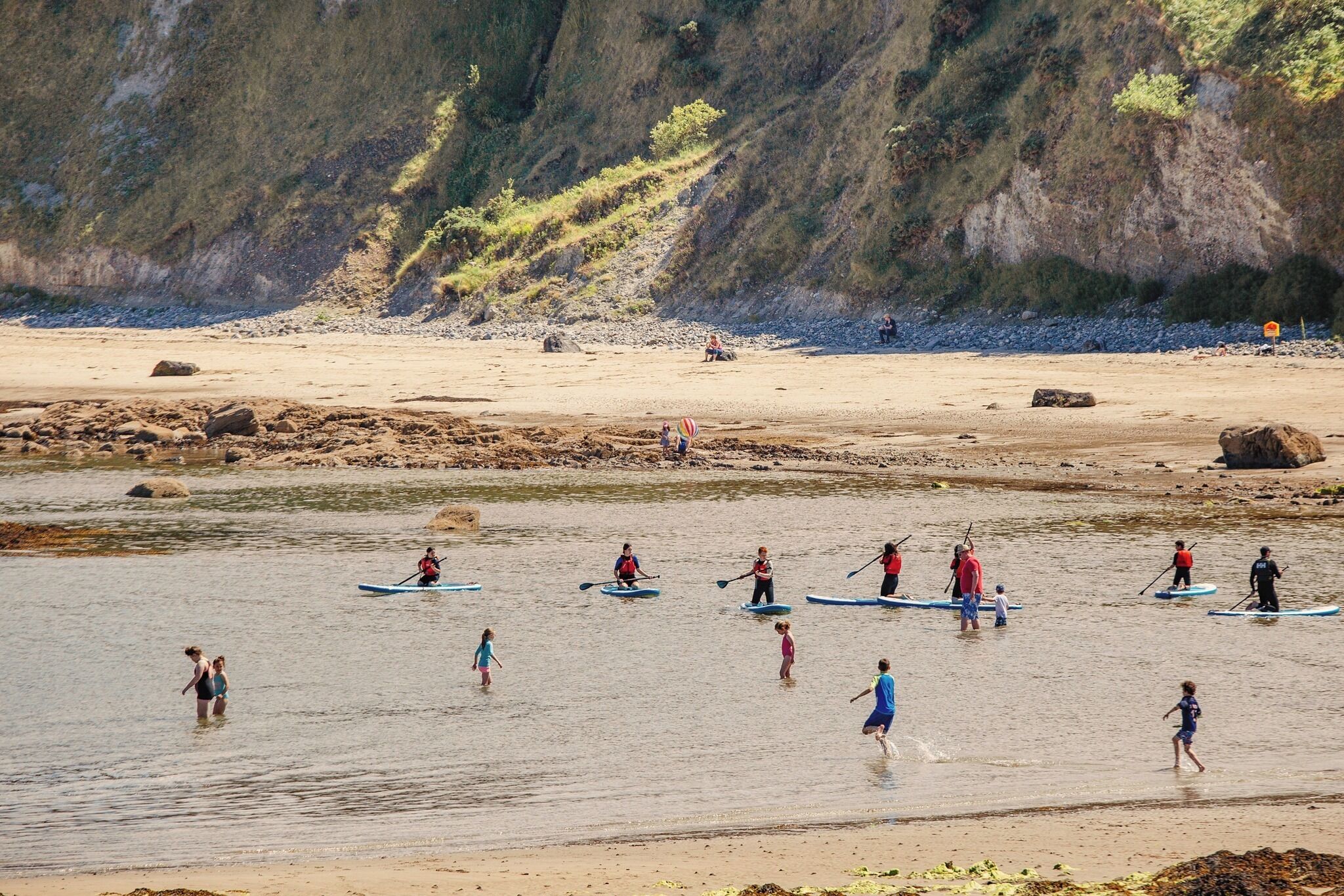 A beach with people paddleboarding and walking along the shore.