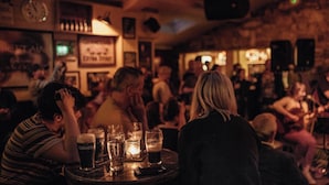 Eine belebte Bar mit Tischen, Gläsern und einer Wanduhr.