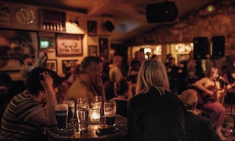 A crowded bar with tables, glasses, and a clock on the wall.