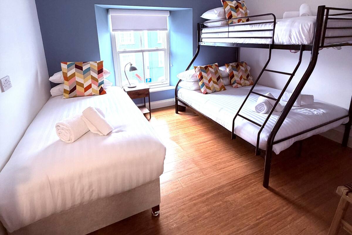 Een kamer met stapelbedden, een bureau, een stoel, een raam met zonwering en uitzicht op het buiten.