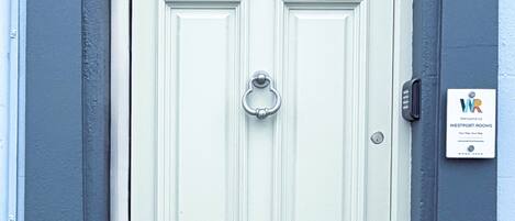 Puerta doble de color claro con mirilla y timbre, enmarcada por paredes oscuras con molduras decorativas.