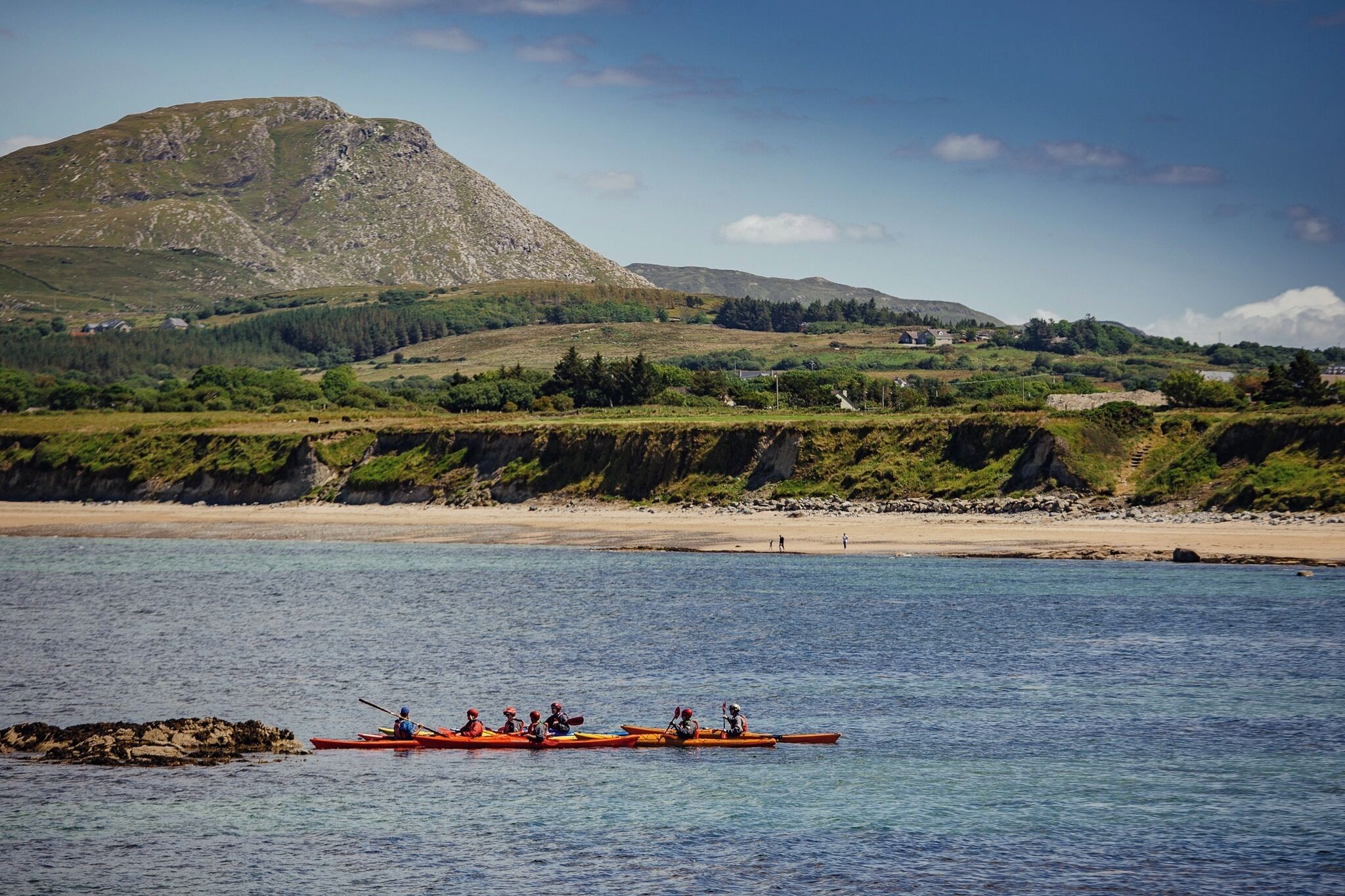 A coastal landscape with a mountain, clear water, and a rowboat with people.