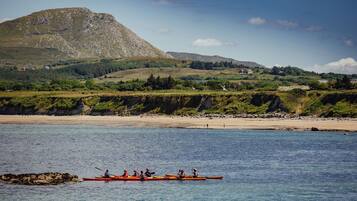 A coastal landscape with a mountain, clear water, and a rowboat with people.