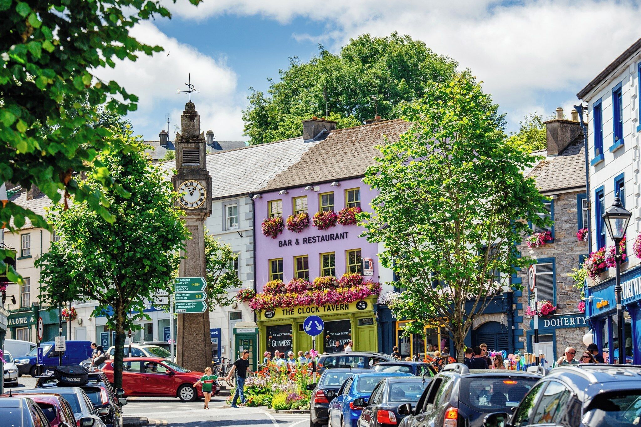 A busy street with a clock tower, a bar and restaurant, and various shops.