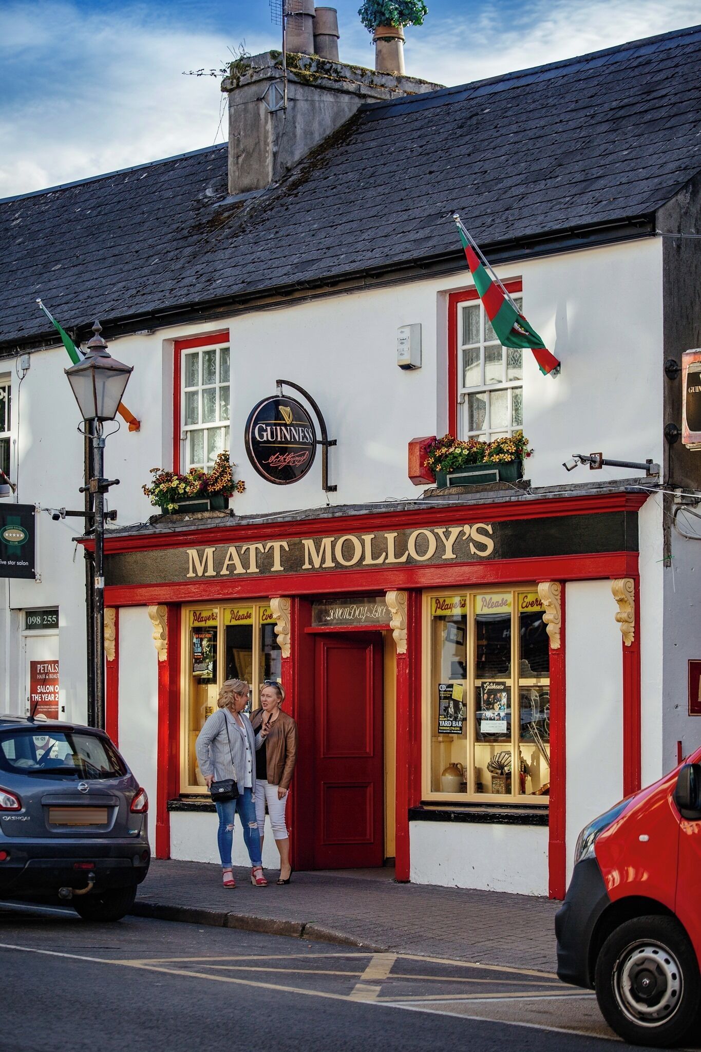 A pub named 'Matt Molloy's' with a Guinness sign, a red door, and a window displaying various items.