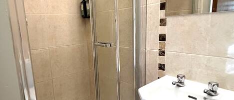 A bathroom with a glass shower enclosure, a white sink, and a mirror.