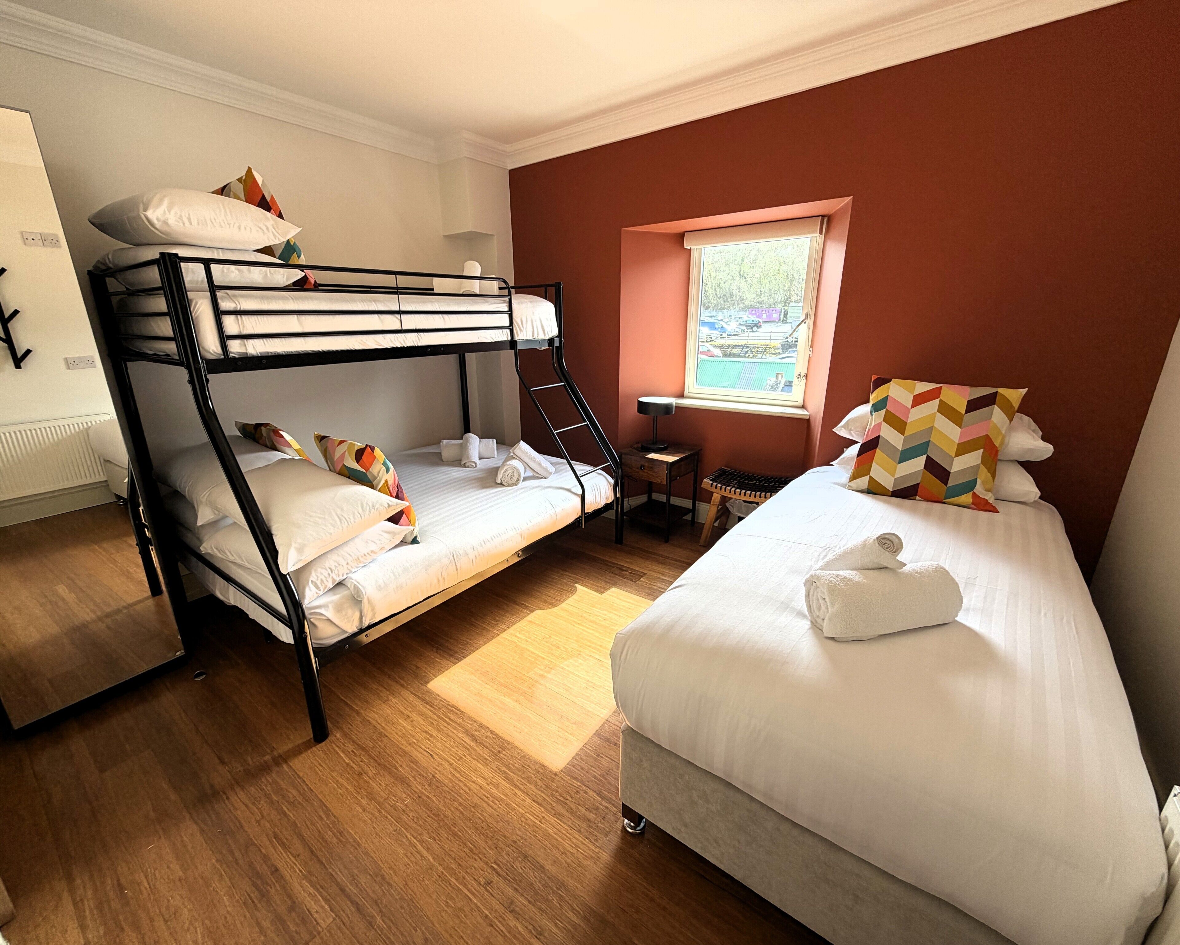 A room with bunk beds, a desk, a chair, and a window.