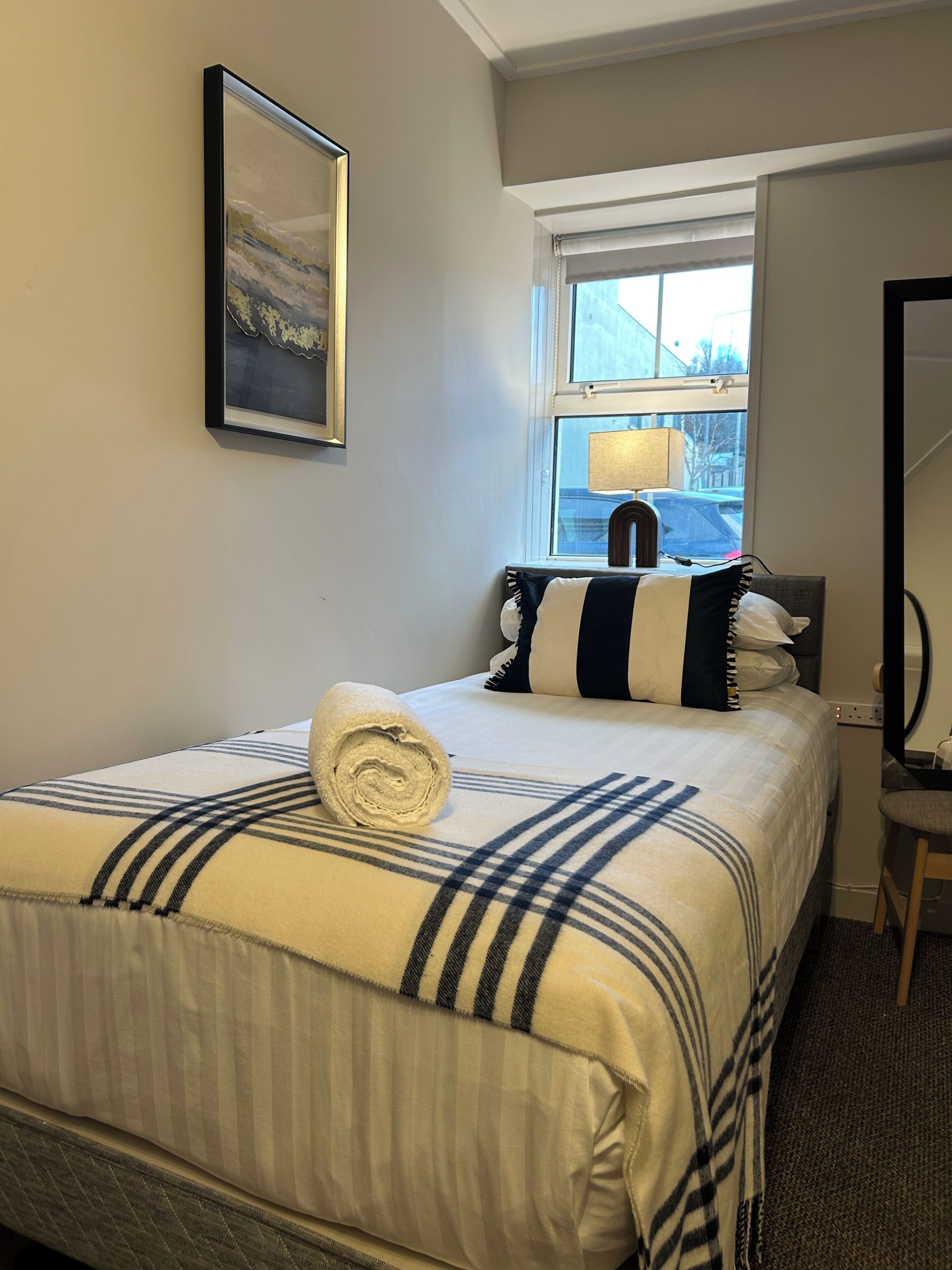 Una habitación de hotel con una cama, una ventana, un cuadro en la pared y una silla.