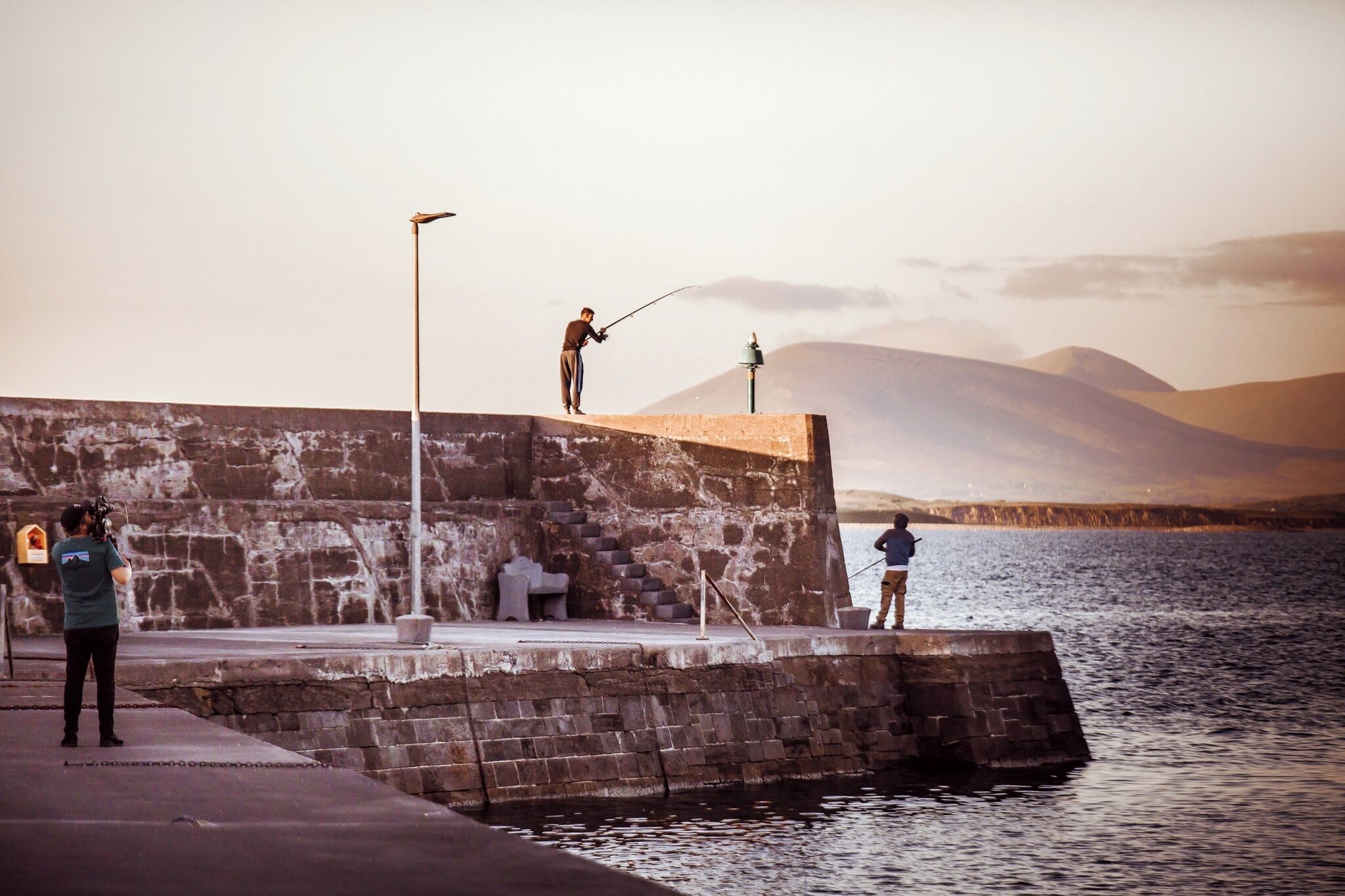 A pier with a stone wall, a lamp post, and a person fishing.