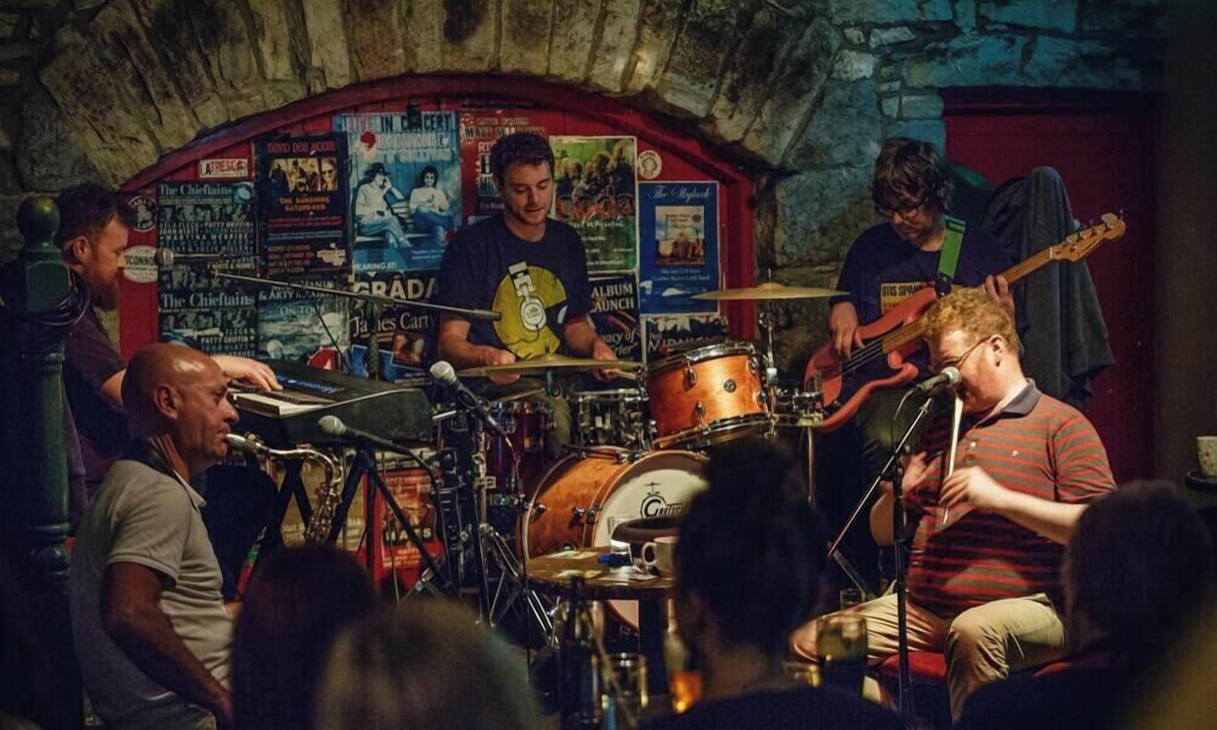 A band performing in a venue with a stone wall and posters.