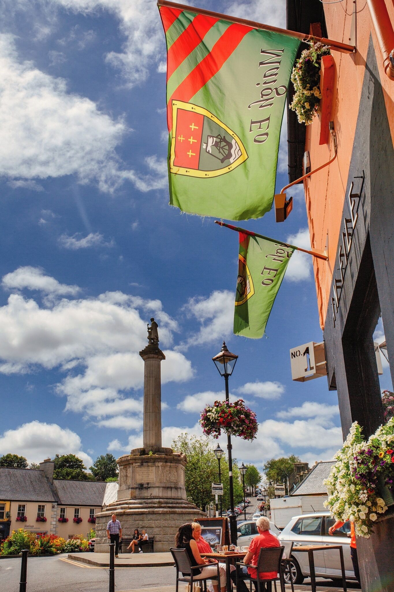 A street scene with a monument, outdoor seating, and flags.