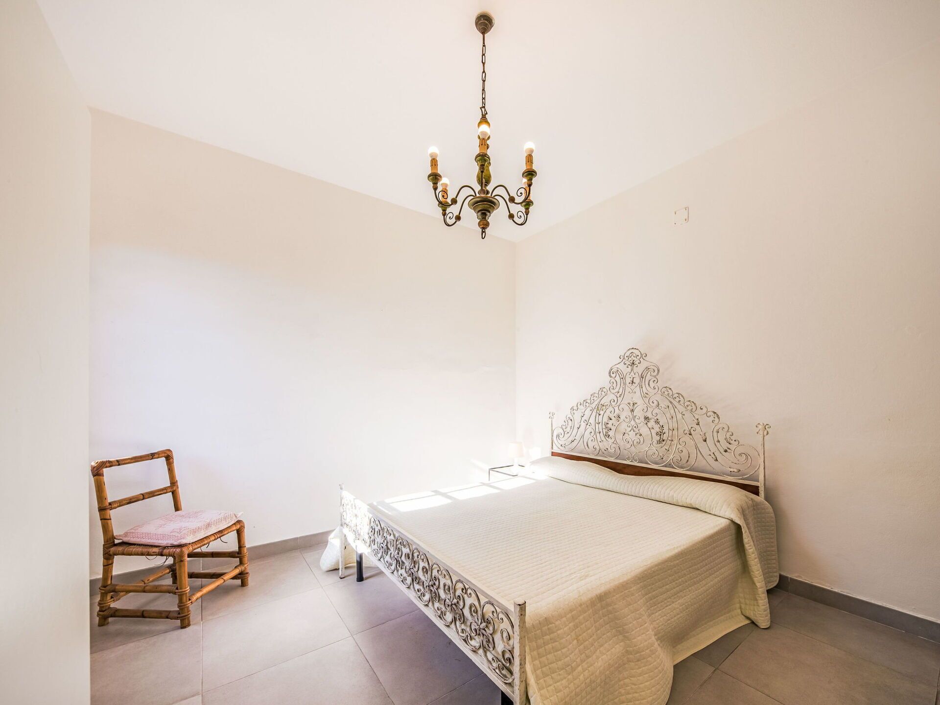 A bedroom with a bed, a chair, and a chandelier.