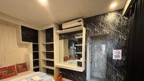 A bedroom with a bed, a vanity with a mirror, built-in shelves, a no-smoking sign, and a bathroom entrance.
