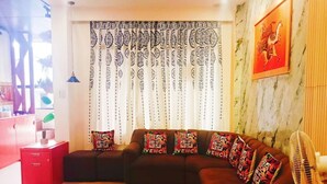 A living room with a sectional sofa, patterned curtains, a wall-mounted artwork, and a red book on a table.