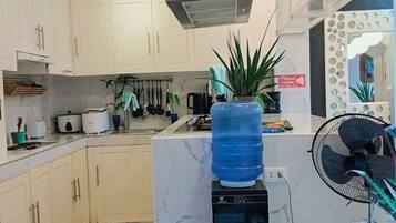 A modern kitchen with white cabinets, a large water dispenser, a fan, and a small rug.
