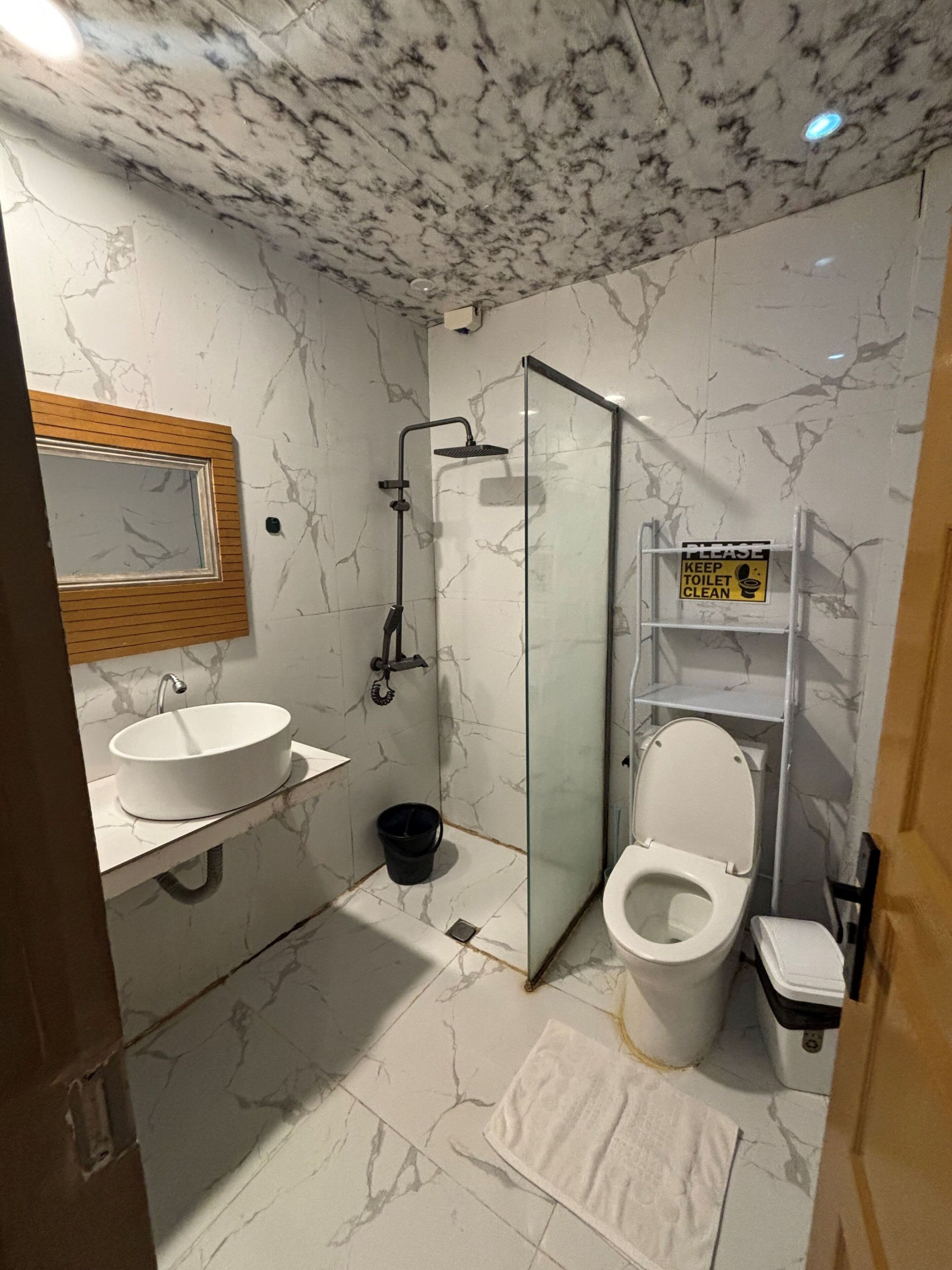 Un baño con piso de mármol, un lavamanos, ducha con cerramiento de vidrio, inodoro y un espejo.