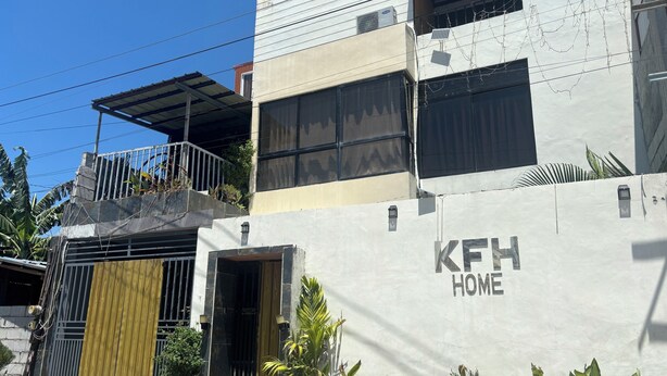 A modern building with a 'KFH HOME' sign, a gated entrance, and a balcony with plants.