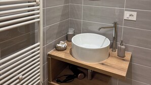 Een badkamer met een witte wastafel, een spiegel, een handdoekhouder en een houten plank met toiletartikelen.