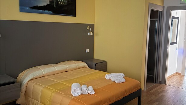 Een hotelkamer met een bed, nachtkastjes, een schilderij aan de muur en een deur naar een andere kamer.