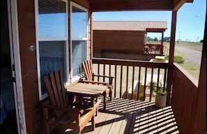 Una terraza de madera con una mesa y sillas, una planta en maceta y vista de un edificio al fondo.
