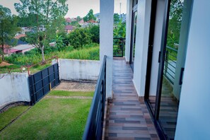 Ein Balkon mit Blick auf eine Rasenfläche und Bäume, einem gefliesten Boden und einem Metallgeländer.