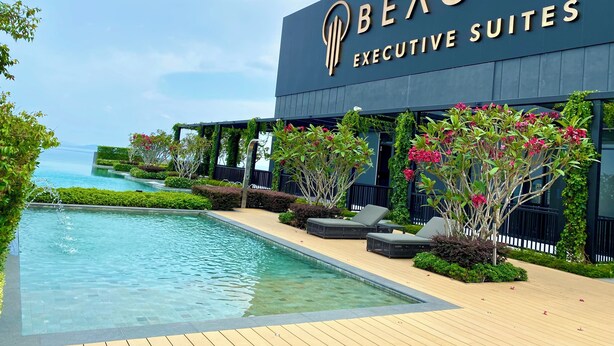 Un hôtel doté d’une piscine, de verdure et d’une enseigne indiquant « BEACON EXECUTIVE SUITES ».