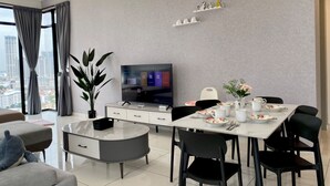 Un salon moderne doté d’un téléviseur à écran plat, d’une table à manger, de chaises, d’un canapé, d’une table basse, d’une plante en pot et offrant une vue sur la ville grâce à de grandes fenêtres.