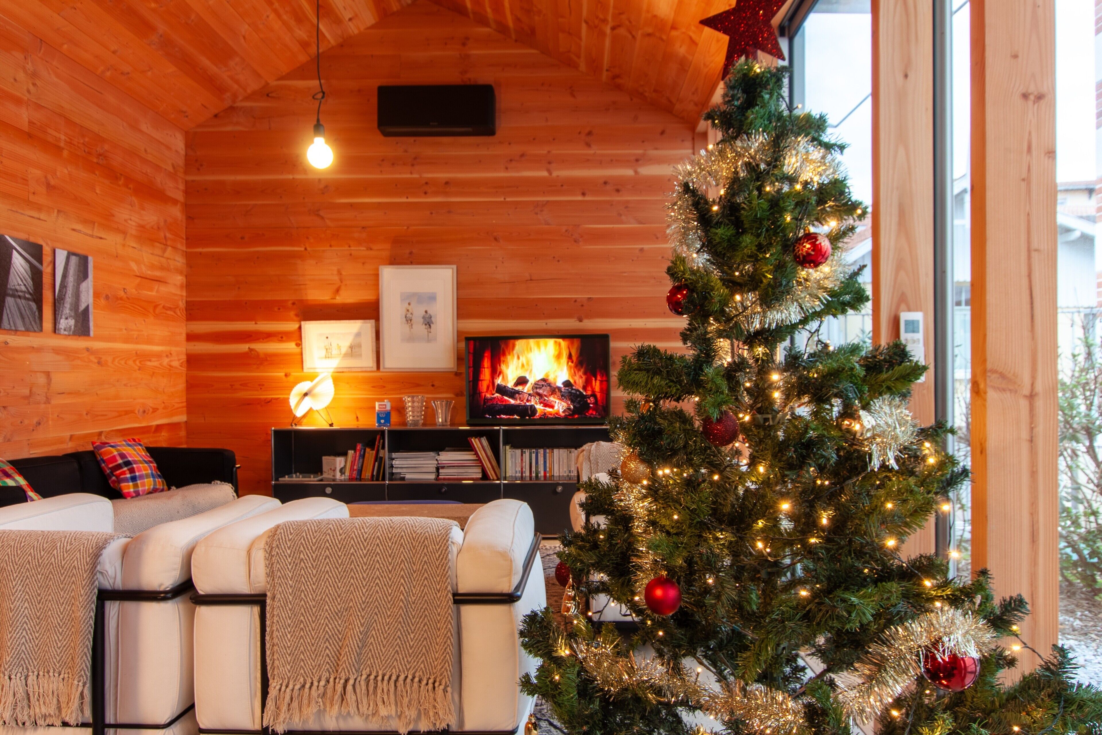 Ein gemütliches Blockhaus-Interieur mit Kamin, Weihnachtsbaum und einer Couch mit Kissen.