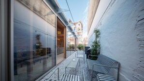A narrow outdoor corridor with benches, a glass wall reflecting interior furnishings, and a building with balconies in the background. - Cabane Cala – Heart of Arcachon & Beaches Within Walking Distance (Arcachon)