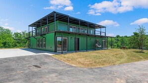 Um edifício moderno de metal verde com varanda coberta, calçada de concreto e uma mesa de piquenique ao fundo.