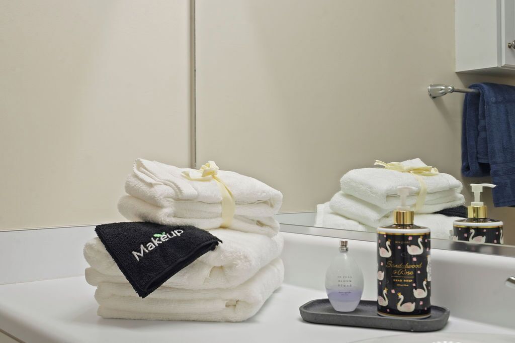 A bathroom with a stack of white towels, a black towel with 'Makeup' written on it, and a hand soap dispenser with swan designs.