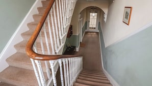 Un escalier avec des balustrades blanches et une main courante en bois, menant à une porte dotée d’un panneau de verre.
