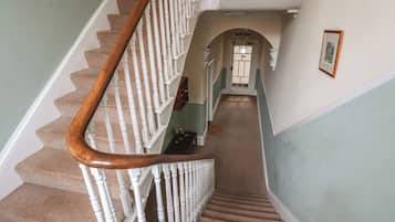 Una escalera con balaustres blancos y barandilla de madera, que conduce a una puerta con un panel de vidrio.