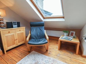 Una habitación con tragaluz, un armario de madera, un sillón de cuero, una mesita con una planta y un cuadro enmarcado.
