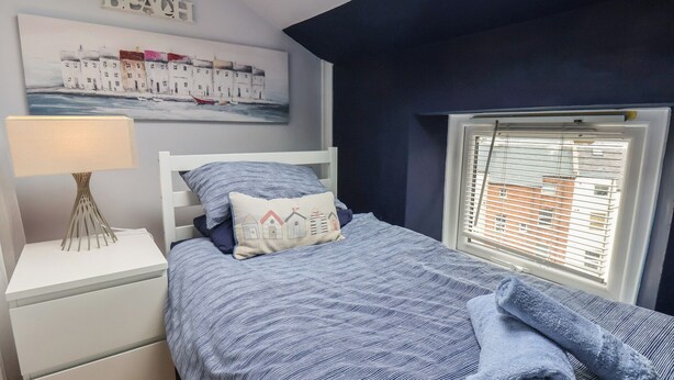 Une chambre à coucher avec un lit, une table de chevet, une lampe, une fenêtre avec des stores et un tableau au mur.